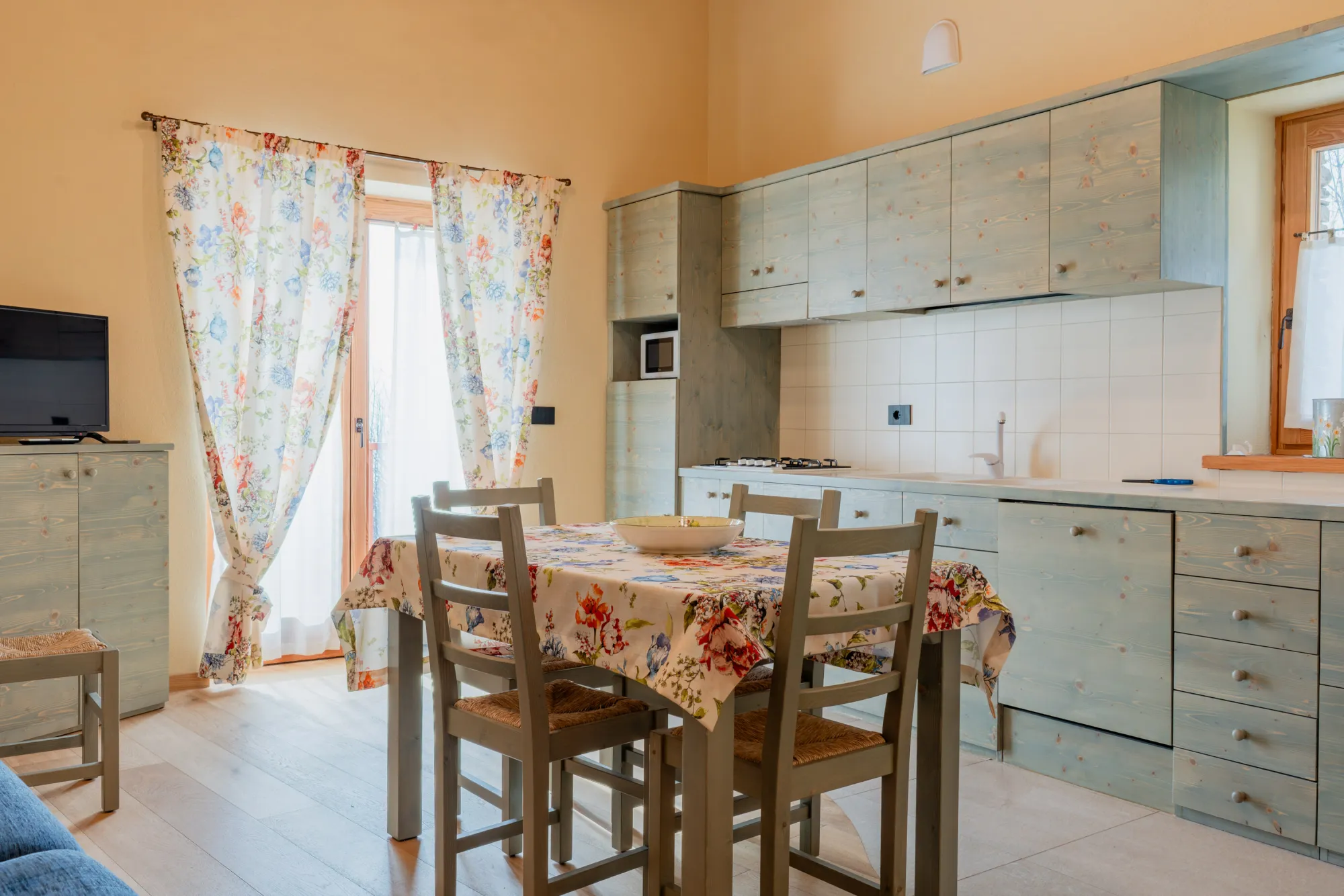 Appartamento Isotta: la cucina verde salvia e il tavolo apparecchiato accanto alla porta-finestra